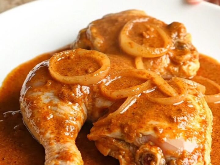 A serving spoon lifting a tender, bone-in chicken thigh coated in a rich, creamy orange paprika sauce from a slow cooker.
