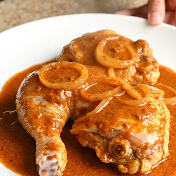 A serving spoon lifting a tender, bone-in chicken thigh coated in a rich, creamy orange paprika sauce from a slow cooker.