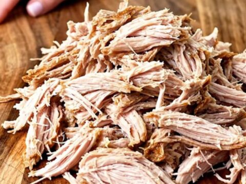 A close-up of tender, shredded BBQ turkey piled high on a wooden board, ready for sliders.