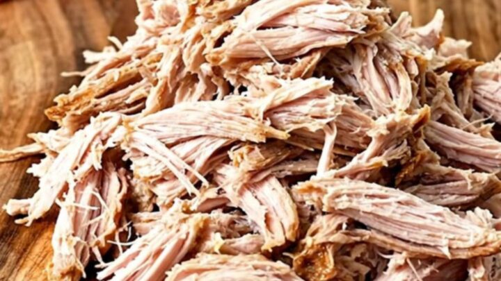 A close-up of tender, shredded BBQ turkey piled high on a wooden board, ready for sliders.