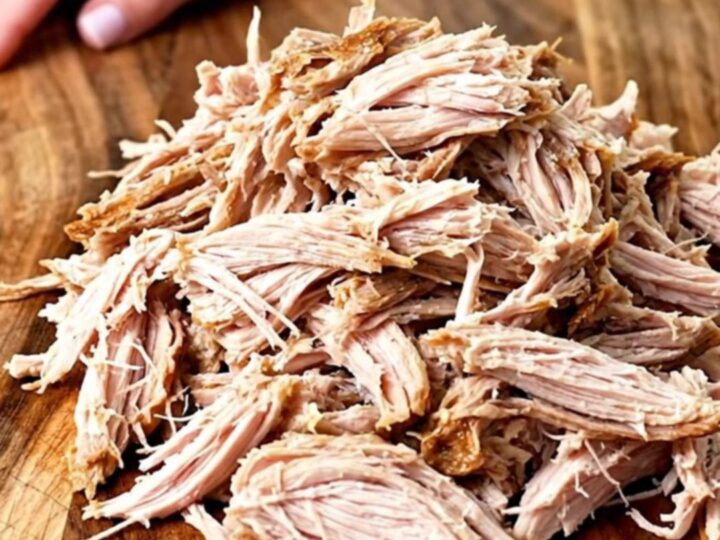 A close-up of tender, shredded BBQ turkey piled high on a wooden board, ready for sliders.