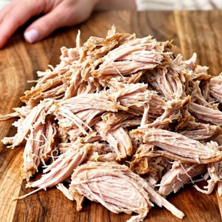 A close-up of tender, shredded BBQ turkey piled high on a wooden board, ready for sliders.