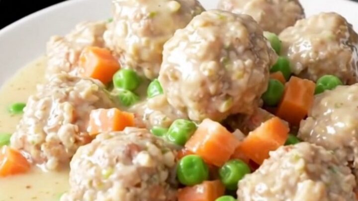A close-up view of creamy chicken pot pie meatballs in a slow cooker, garnished with peas and carrots.