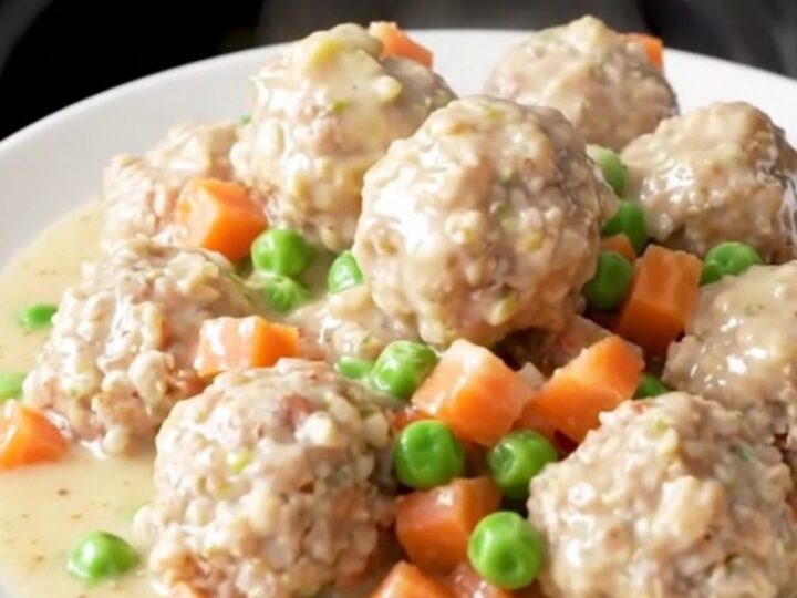 A close-up view of creamy chicken pot pie meatballs in a slow cooker, garnished with peas and carrots.