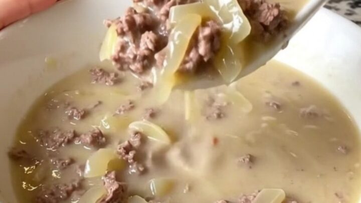 A warm bowl of creamy patty melt soup with visible ground beef, onions, and melted Swiss cheese.