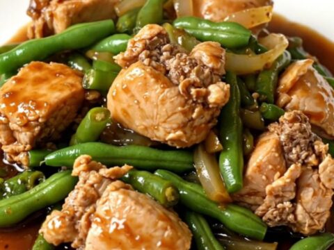 A top-down view of a slow cooker filled with cooked chicken chunks, green beans, and onions in a dark ginger-soy glaze.