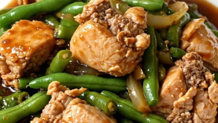 A top-down view of a slow cooker filled with cooked chicken chunks, green beans, and onions in a dark ginger-soy glaze.
