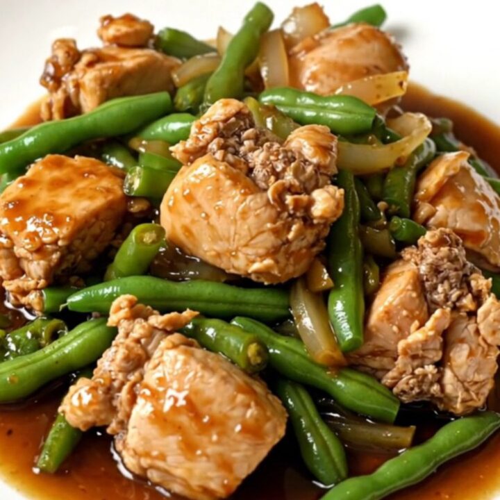 A top-down view of a slow cooker filled with cooked chicken chunks, green beans, and onions in a dark ginger-soy glaze.