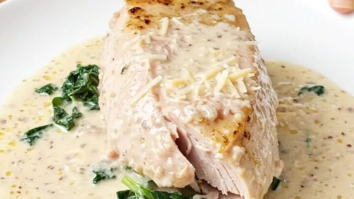 A close-up of tender, cooked turkey breast topped with creamy parmesan sauce and wilted spinach.