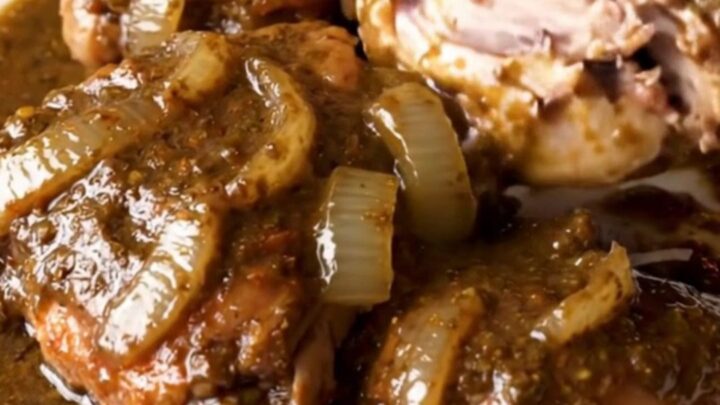 A close-up view of succulent, shredded turkey thighs coated in a rich, dark mole sauce in a slow cooker.