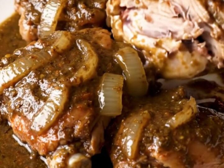 A close-up view of succulent, shredded turkey thighs coated in a rich, dark mole sauce in a slow cooker.