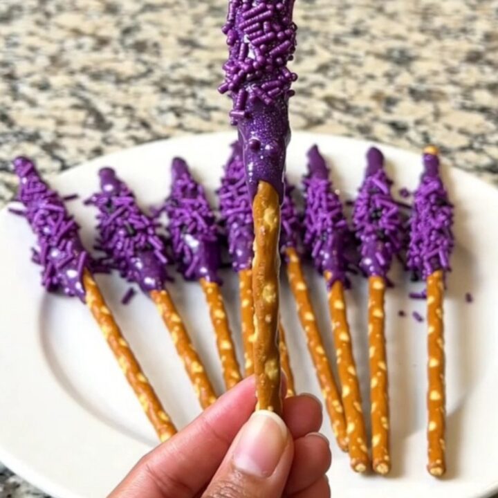 A dozen purple-dipped witch wand pretzel rods arranged neatly on a dark baking sheet.