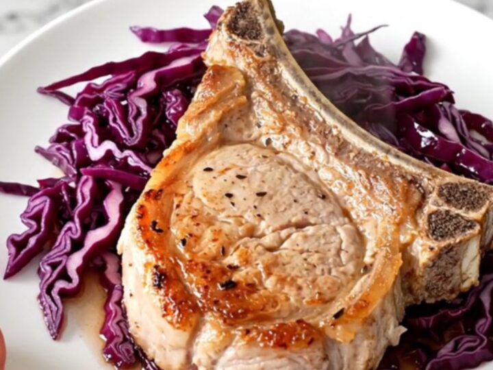 A close-up of a tender bone-in pork chop served over a bed of deep purple braised cabbage and sliced apples.