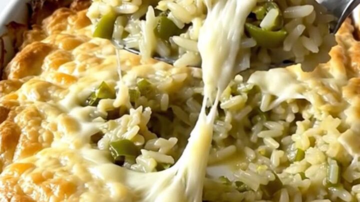 A top-down view of a rectangular ceramic dish filled with creamy green chile rice topped with melted Monterey Jack cheese.
