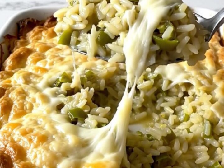 A top-down view of a rectangular ceramic dish filled with creamy green chile rice topped with melted Monterey Jack cheese.