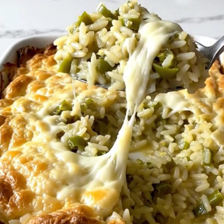 A top-down view of a rectangular ceramic dish filled with creamy green chile rice topped with melted Monterey Jack cheese.