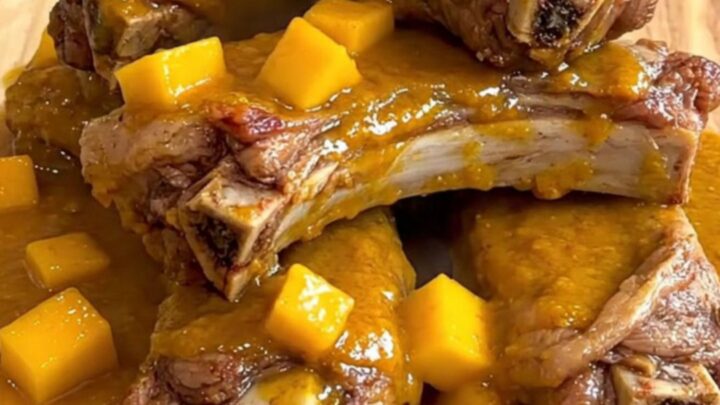 A close-up of tender, glazed pork spareribs arranged on a wooden board, coated in a thick, vibrant mango habanero sauce.