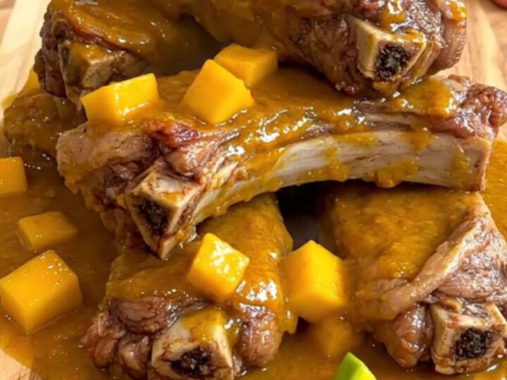 A close-up of tender, glazed pork spareribs arranged on a wooden board, coated in a thick, vibrant mango habanero sauce.