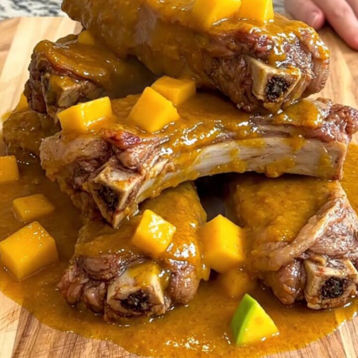 A close-up of tender, glazed pork spareribs arranged on a wooden board, coated in a thick, vibrant mango habanero sauce.