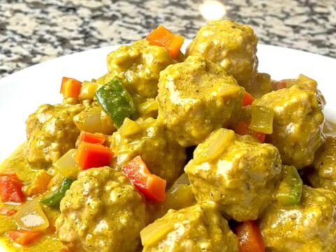 A bowl filled with tender chicken meatballs coated in a creamy yellow coconut curry sauce.