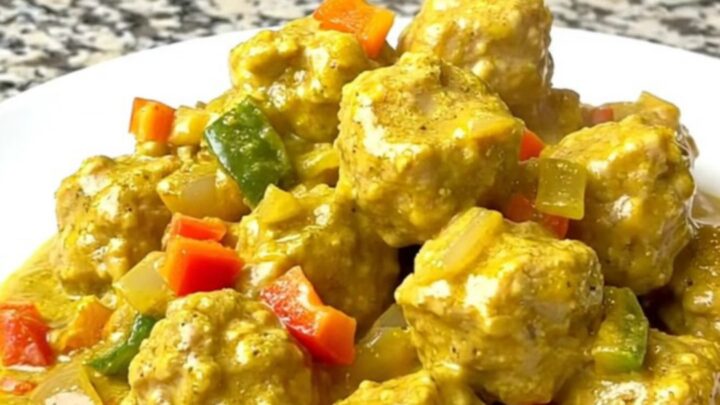A bowl filled with tender chicken meatballs coated in a creamy yellow coconut curry sauce.