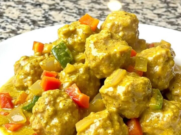 A bowl filled with tender chicken meatballs coated in a creamy yellow coconut curry sauce.