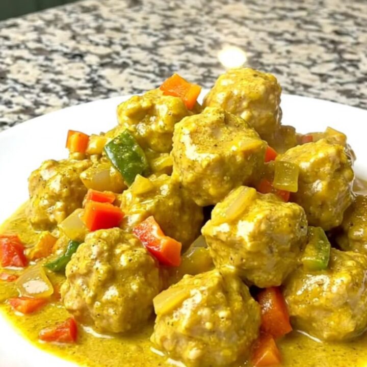 A bowl filled with tender chicken meatballs coated in a creamy yellow coconut curry sauce.
