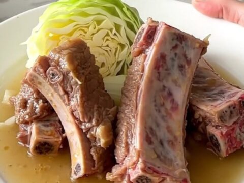 A close-up of tender braised country-style pork ribs served with soft cabbage wedges and onions in a savory broth.