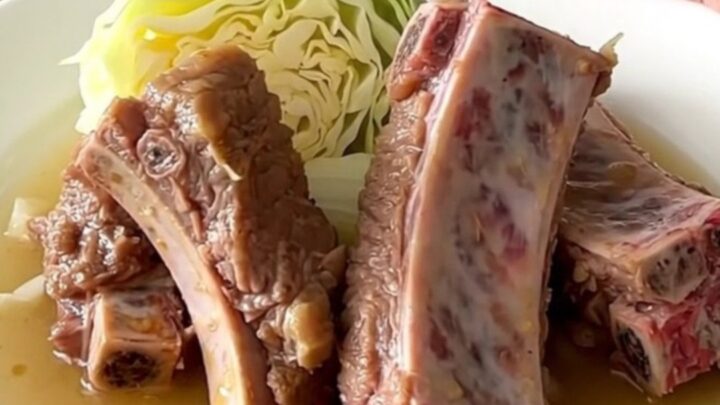 A close-up of tender braised country-style pork ribs served with soft cabbage wedges and onions in a savory broth.