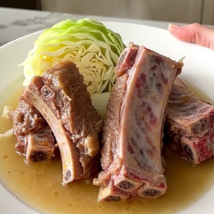 A close-up of tender braised country-style pork ribs served with soft cabbage wedges and onions in a savory broth.