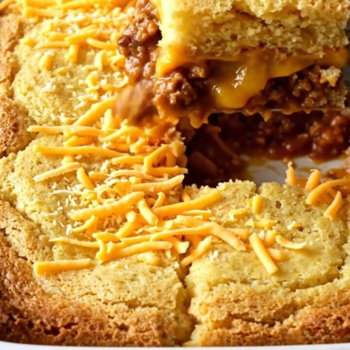 A golden, freshly baked turkey chili cornbread bake in a ceramic dish, with melted cheddar on top.