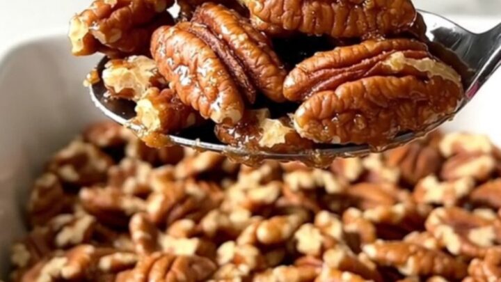 A large ceramic dish filled with golden toasted cinnamon sugar candied pecans on a white countertop.