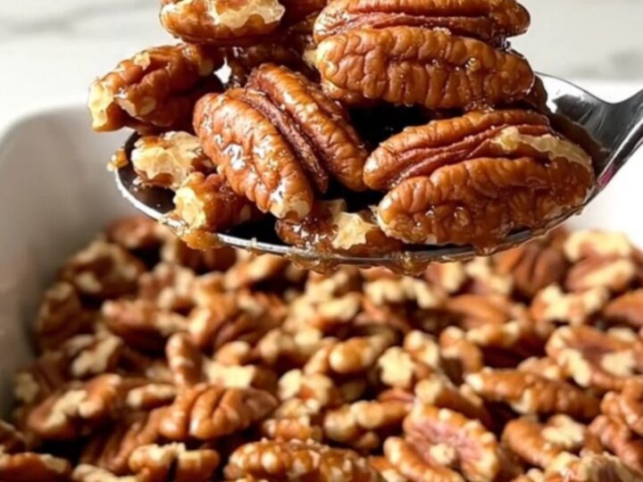A large ceramic dish filled with golden toasted cinnamon sugar candied pecans on a white countertop.