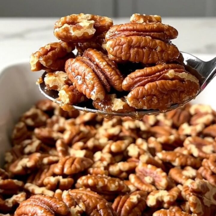 A large ceramic dish filled with golden toasted cinnamon sugar candied pecans on a white countertop.