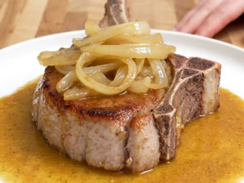 Four bone-in pork chops in a slow cooker covered with onions and a rich, buttery sauce.