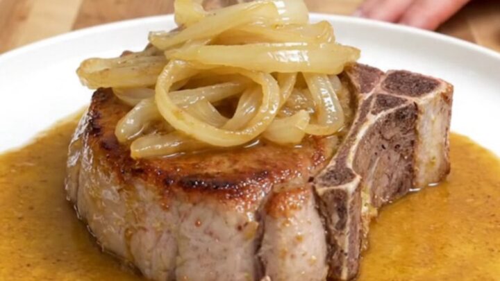 Four bone-in pork chops in a slow cooker covered with onions and a rich, buttery sauce.