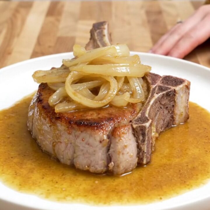 Four bone-in pork chops in a slow cooker covered with onions and a rich, buttery sauce.