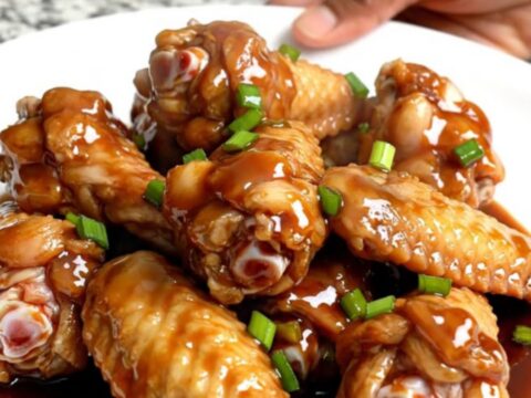 A top-down view of raw chicken wings packed into a black slow cooker insert on a speckled granite countertop.