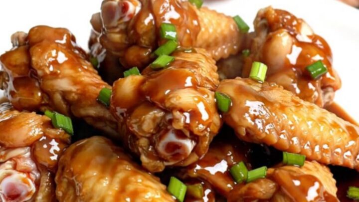 A top-down view of raw chicken wings packed into a black slow cooker insert on a speckled granite countertop.