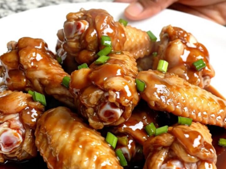 A top-down view of raw chicken wings packed into a black slow cooker insert on a speckled granite countertop.