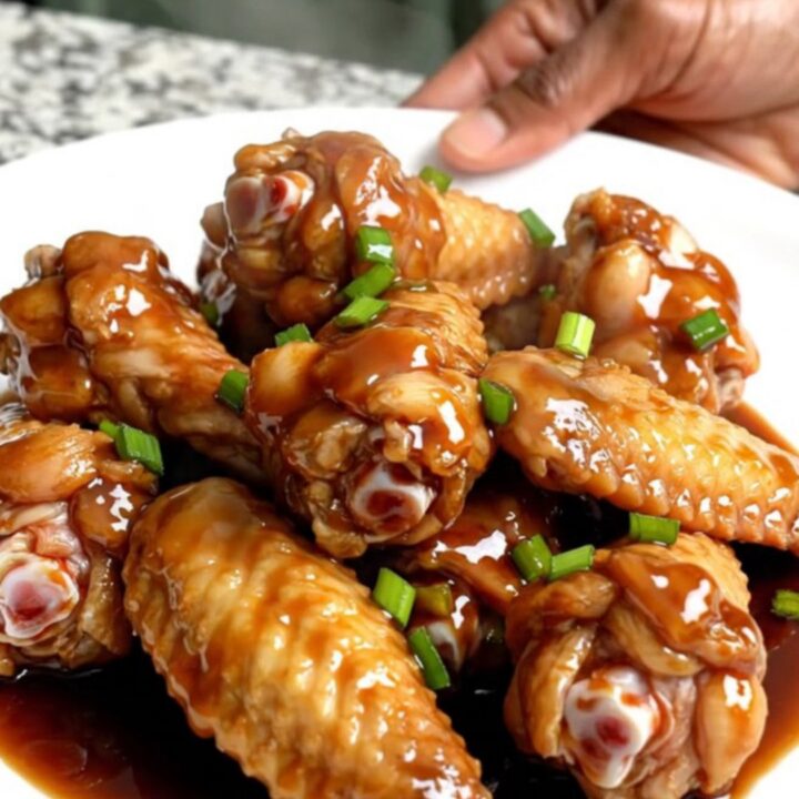 A top-down view of raw chicken wings packed into a black slow cooker insert on a speckled granite countertop.