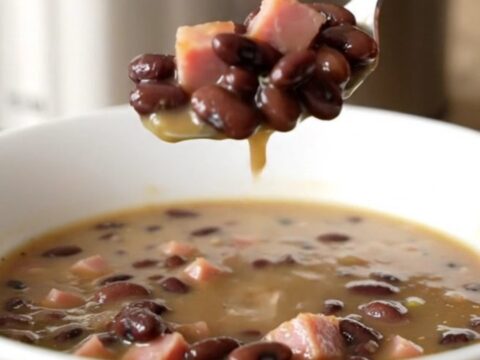 A close-up of a slow cooker filled with black bean and ham soup on a beige countertop.