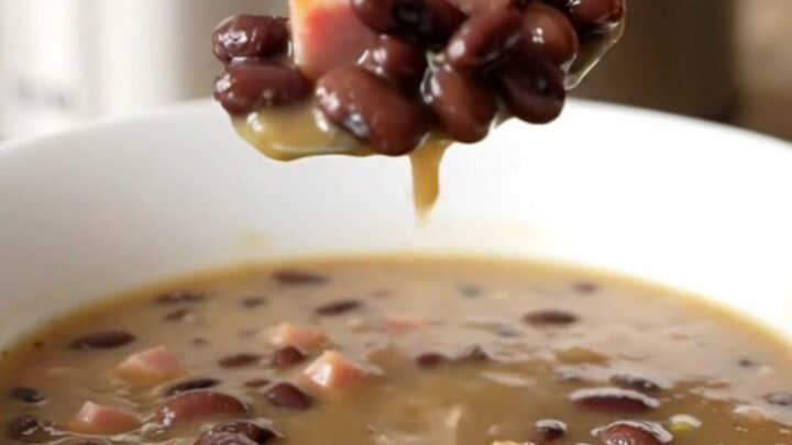 A close-up of a slow cooker filled with black bean and ham soup on a beige countertop.