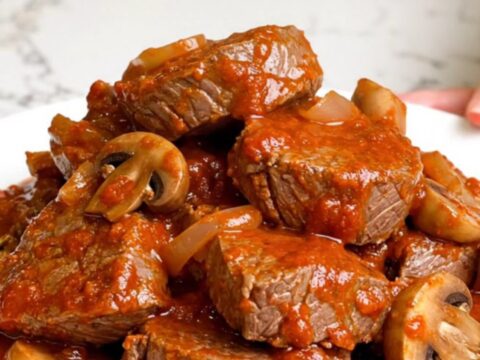 A slow cooker filled with tender round steak pieces and mushrooms in a rich, red marinara sauce.