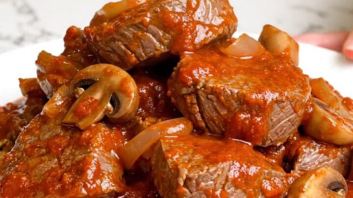 A slow cooker filled with tender round steak pieces and mushrooms in a rich, red marinara sauce.