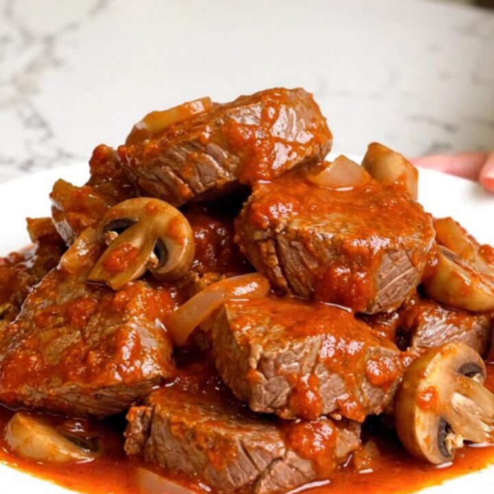 A slow cooker filled with tender round steak pieces and mushrooms in a rich, red marinara sauce.