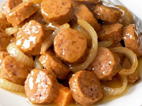 A close-up of a slow cooker filled with golden-brown chicken sausage coins, tender sweet potato cubes