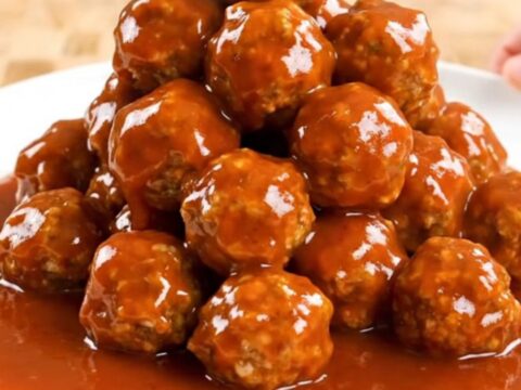 A close-up of firecracker turkey meatballs in a slow cooker, coated in a thick, vibrant orange-red sauce.