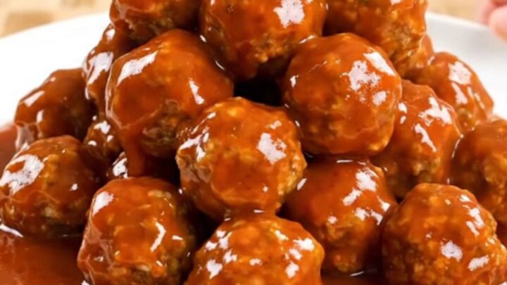 A close-up of firecracker turkey meatballs in a slow cooker, coated in a thick, vibrant orange-red sauce.