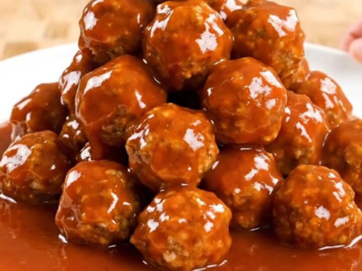 A close-up of firecracker turkey meatballs in a slow cooker, coated in a thick, vibrant orange-red sauce.